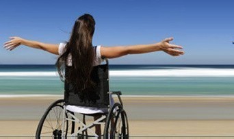 Frau im Rollstuhl am Meer mit weit ausgebreiteten Armen – Sinnbild für Freiheit und Mobilität